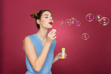 Attractive young woman in blue dress standing and blowing bubbles