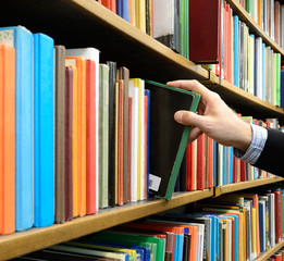 Obraz premium Hand picking book in library bookshelf