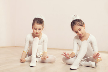 Little ballerinas sitting on the floor and adjusting slippers © johoo