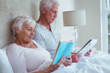 Senior couple reading book on bed