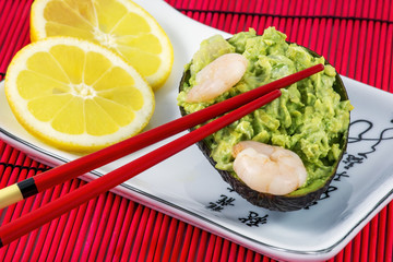 Tasty avocado salad with shrimps, lemon and red chopsticks on the white plate