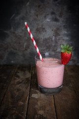 Getränk aus Erdbeeren in einem Glas mit Trinkhalm auf einem alten Holzuntergrund