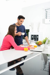 young couple at home having coffee in kitchen and working on laptop computer