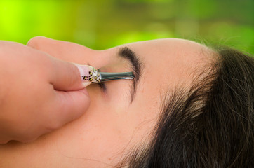 Obraz premium Closeup woman headshot profile,lying with eyes closed and hand holding tweezer pulling eyebrow