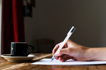 Hand writing with a pen. Coffee at a wooden table. Selective focus.