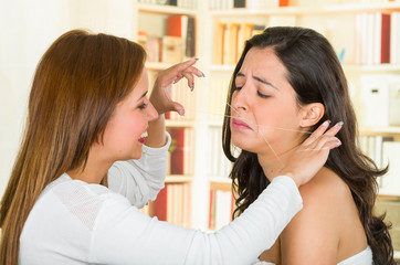 Cosmetologist performing facial hair removal using threading technique on brunette patient with painful face expressions