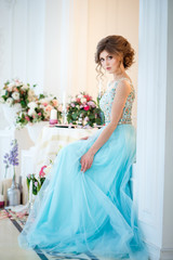 Fototapeta premium Beautiful young lady in a luxury blue dress in elegant interior decorated with flowers