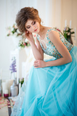 Beautiful young lady in a luxury blue dress in elegant interior decorated with flowers