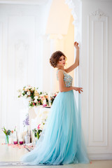 Beautiful young lady in a luxury blue dress in elegant interior decorated with flowers