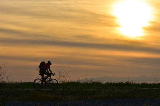 Cyclist on sunset sky with clouds 