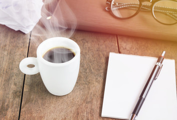 White cup of black coffee with blank note book and pencil on woo