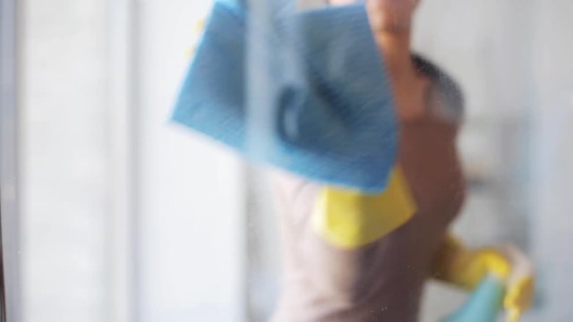 woman in gloves cleaning window with rag and spray