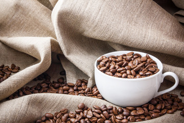 White cup with coffee seeds inside on linen fabric.