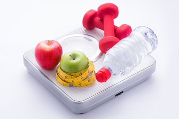 Weight scale, healthy snack, measuring tape and dumbbells on a table, weight loss and sports concept, flat lay