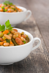 White beans with vegetables in a bowl on wood