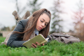 Obraz premium Beautiful girl writing in a book / Girl student in park writes in writing book