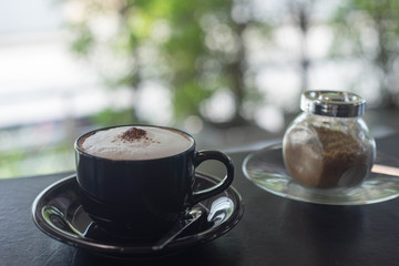 hot cappuccino in black coffee glass on black table
