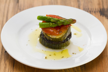 eggplant with zucchini, tomato, asparagus and pepper on white plate on brown background
