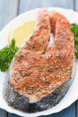 fresh salmon with herbs and lemon on white dish on blue wooden background