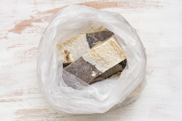 dry salted cod fish in plastic bag on white wooden background