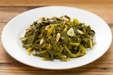 boiled greens with nuts and garlic on white plate on brown wooden background