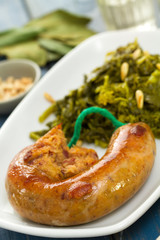 traditional portuguese smoked sausage with greens on white plate and glass of white wine