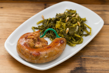 traditional portuguese smoked sausage with turnip greens on white plate on brown background