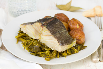 boiled cod fish with potato and greens on white plate on white wooden background