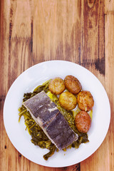 boiled cod fish with potato and greens on white plate on brown wooden background