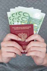 female hand holding a passport with Euro banknotes.