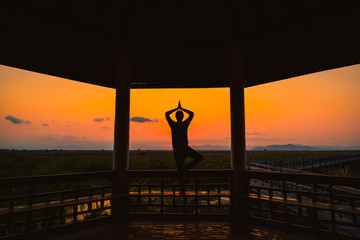 Silhouette young man playing yoga on wooden pagoda in park at sunset