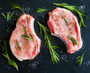 Raw pork steaks with rosemary on black stone background. Top view.