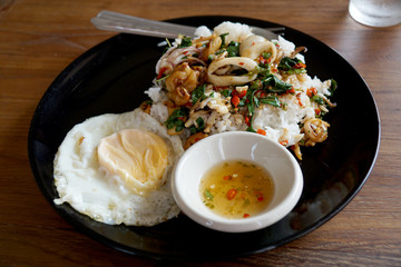 Rice topped with spicy fried squid, basil leaves and fried egg (Thai food)