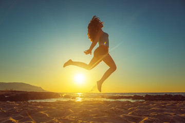 Happy girl jumping on the beach against beautiful sunset