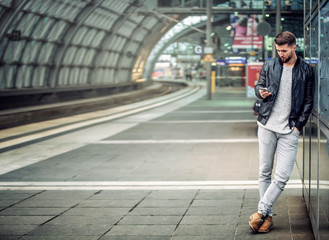 Junger Mann mit Smartphone im Bahnhof