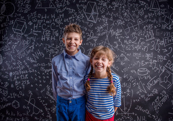 Happy boy and girl at school against big blackboard.