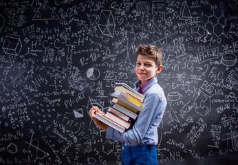 Boy with books against big blackboard with mathematical symbols