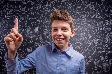 Boy with raised finger against big blackboard with formulas