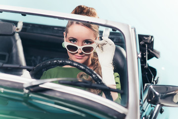 Vintage 1960 woman in convertible car looking over sunglasses.