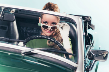 Vintage 1960 woman in convertible car looking over sunglasses. - obrazy, fototapety, plakaty