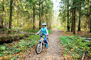 Naklejka premium Little girl riding on bicycle in the forest
