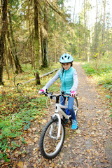 Fototapeta premium Little girl riding on bicycle in the forest