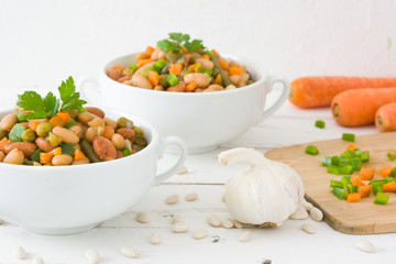White beans with vegetables on white wood
