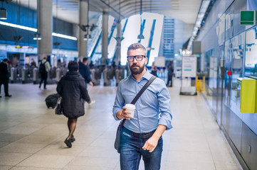 Hipster businessman with coffee cup walking in subway station