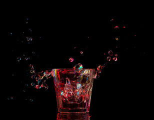 Bright cocktail in glass and splashing water on dark background