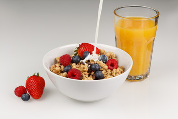 Müsil mit Organgensaft und eingießender Milch, Erdbeeren, Heidelbeeren und Himbeeren