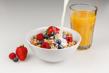 Müsil mit Organgensaft und eingießender Milch, Erdbeeren, Heidelbeeren und Himbeeren