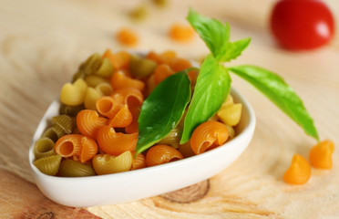 Dry multicolored gomiti pasta in white bowl on wooden table