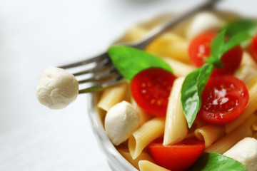 Cooked penne pasta with mozzarella, fresh tomatoes and basil in white bowl, close up