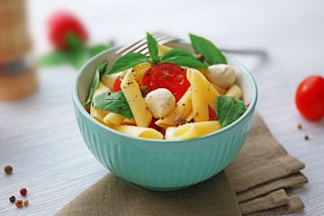 Cooked penne pasta with mozzarella, fresh tomatoes and basil in blue bowl on wooden table
